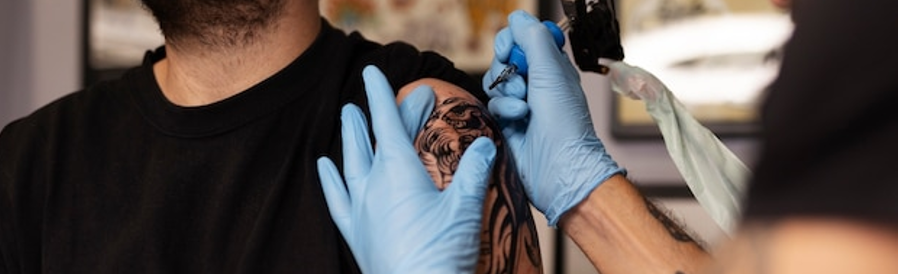 Tatoeëerder zet een tattoo op linkerbovenarm van meneer